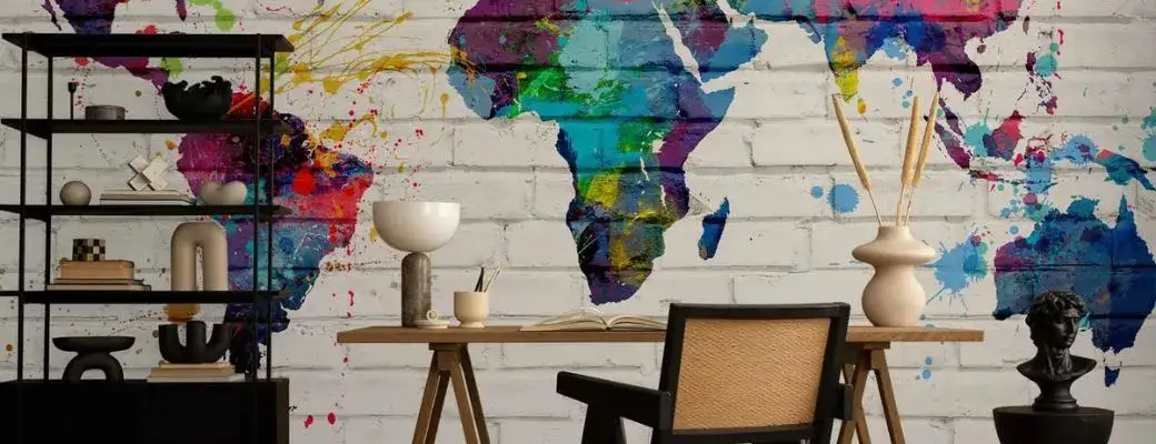 Colourful wall mural with a world map on a white brick wall in a home office A modern office with a wall mural imitating a white brick wall, on which a world map has been painted in the style of colourful, expressive splashes of paint. Against the wall stands a minimalist desk, with a chair with a backrest in front of it.